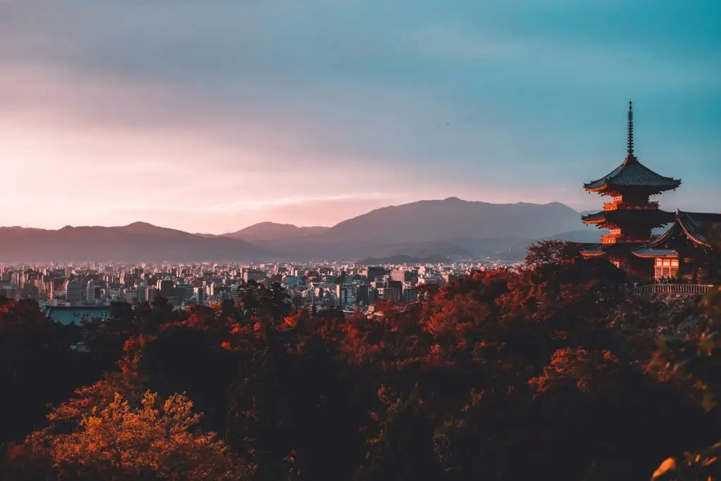 sun peeking over the mountains and city in the distance, with a temple in the foreground