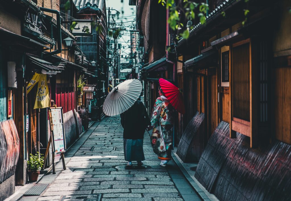two people walking on a stone street with parasols in Kyoto Japan
