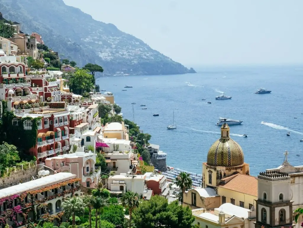 View over Amalfi overlooking a collection of buildings and the blue water filled with yachts and sailboats with the coastline in background