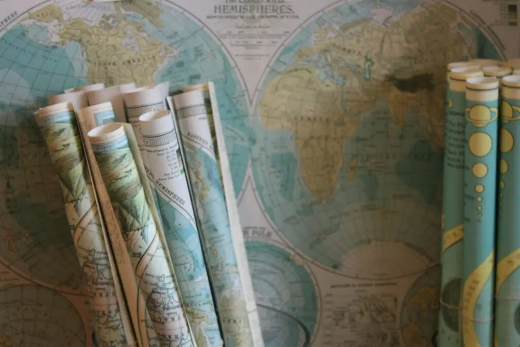 Maps rolled up and set in front of a map hanging on a wall, all ready for exploration and planning a global journey