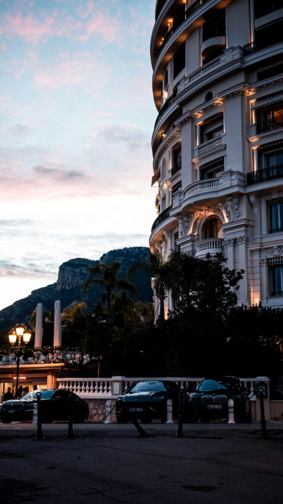 sunset in Monaco with blue and pink sky behind dark building lit with ambient lighting and luxury cars parked out frong
