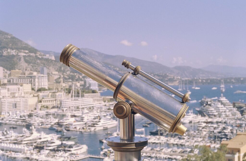 Tourist telescope in front of the shoreline of Monaco with white buildings and blue sea in the background