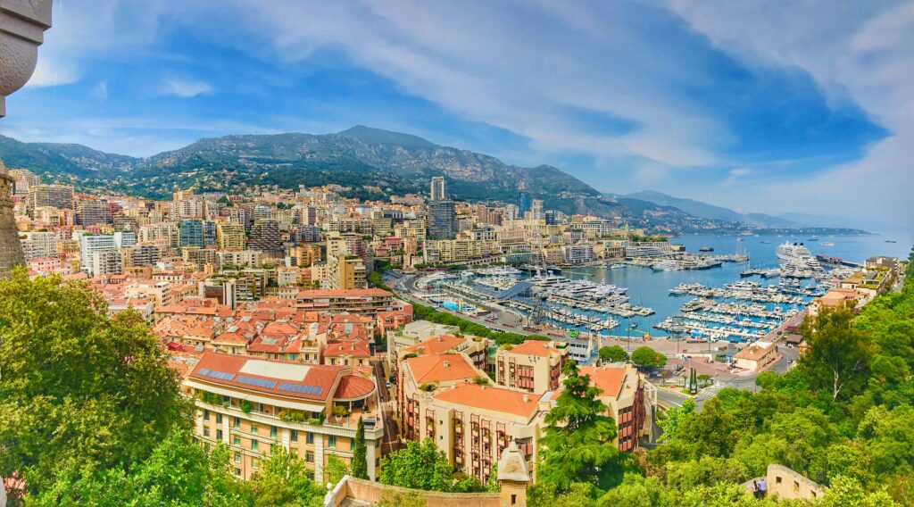 The shoreline of Monaco seen from a hillside looking down over green trees, orange roofs and onto the blue waters